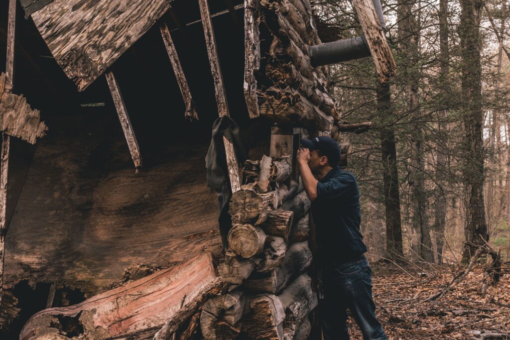 A person looking in the window of an abandoned building in the woods/